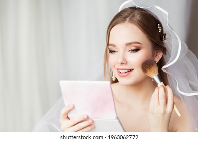 Bride Face Make up Finish. Bridal Wedding Makeup Close up. Skin Foundation Application. Happy Beauty Model holding Blush Brush looking at Mirror. Perfect Smooth Skin Color Texture