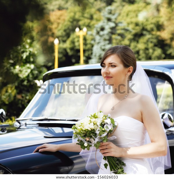 Bride with flowers standing at the car and\
looking sideways