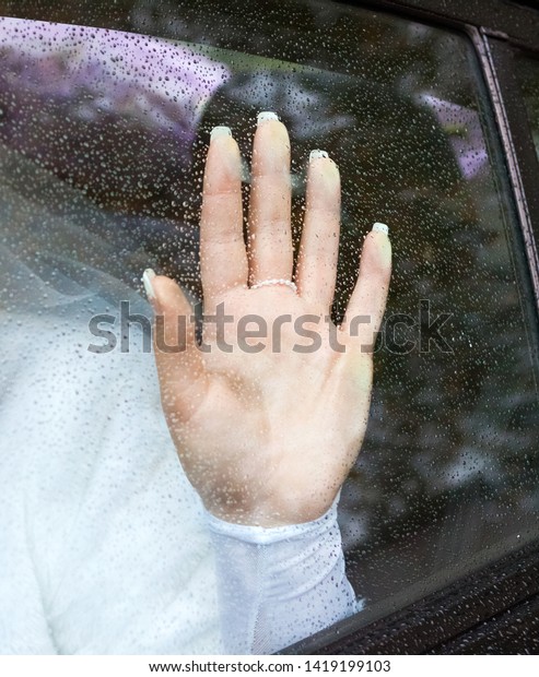 the bride folded her hands on glass of the car
window during the rain