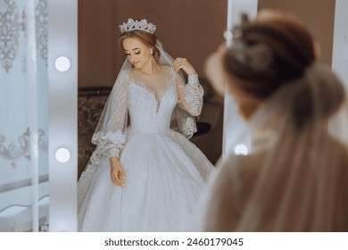 A bride is getting ready for her wedding and is looking at herself in the mirror. She is wearing a white dress and a tiara