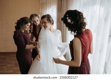 A bride is getting ready for her wedding with her bridesmaids. The bride is wearing a white dress and the bridesmaids are wearing red dresses. They are all smiling and looking happy - Powered by Shutterstock