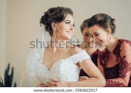 A bride is getting ready for her wedding with her bridesmaids. She is wearing a white dress and a veil. The bridesmaids are helping her get ready and are smiling. Scene is happy and celebratory