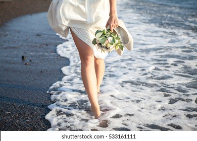 The bride goes barefoot in the sea surf. Carries wedding bouquet and shoes.The Island Of Santorini. Greece.