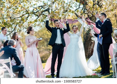 Bride And Groom After Wedding Ceremony. The Master Of Ceremonies Reads From A Sheet Beautiful Words To Newlyweds Who Are Standing In Green Sunny Park. Stylish Happy Smiling Newlyweds On The Outdoor