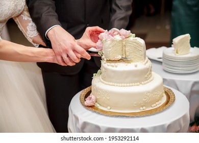 The bride and groom at the banquet together cut the wedding cake, holding on to one knife. Wedding details close-up