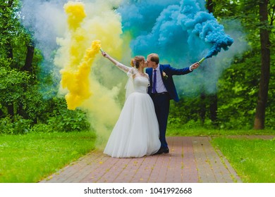 Bride And Groom With The Blue And Yellow Colored Smoke Bombs In The Summer Park