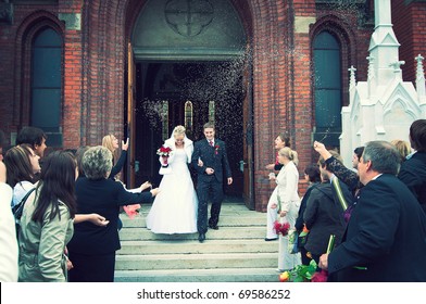 Bride And Groom At Church Door With Rice Confetti Being Thrown