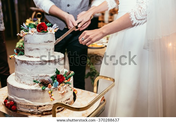 bride and groom cut rustic wedding cake\
on wedding banquet with red rose and other\
flowers