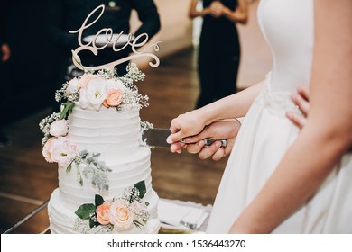 Bride and groom cutting stylish wedding cake at wedding reception in restaurant. Wedding couple holding knife and cutting together wedding cake decorated with flowers - Powered by Shutterstock
