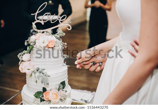Bride and groom\
cutting stylish wedding cake at wedding reception in restaurant.\
Wedding couple holding knife and cutting together wedding cake\
decorated with flowers