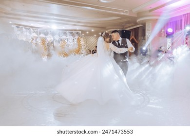 A bride and groom are dancing in a ballroom with a fog machine. The bride is wearing a white dress and the groom is wearing a suit. The fog machine creates a misty atmosphere, adding to the romantic - Powered by Shutterstock