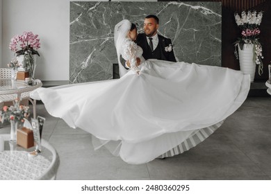 A bride and groom are dancing together in a room with a green wall. The bride is holding her husband's hand and is wearing a white dress - Powered by Shutterstock