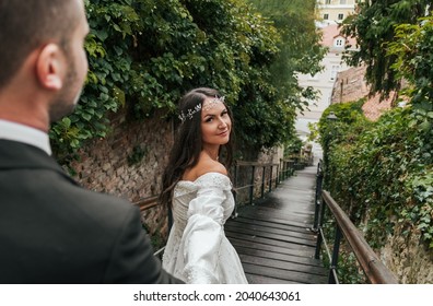 Bride And Groom Doing Wedding Photo Shoot On Wooden Stairs Surrounded By Green Plants At Gornji Grad In Zagreb, Croatia 