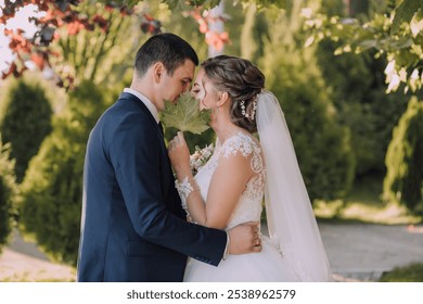 A bride and groom are embracing each other in a garden. The bride is wearing a white dress and the groom is wearing a blue suit - Powered by Shutterstock