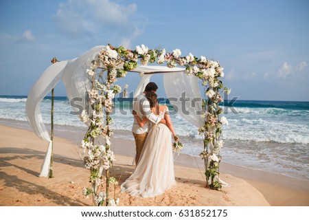 Bride and groom enjoying beach wedding in tropics,  wedding arch, ocean background