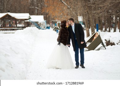 The Bride And Groom Fight Hands And Kiss In A Winter Park. Winter Wedding.