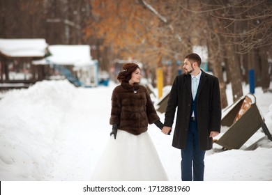 The Bride And Groom Fight Hands And Stroll Through The Winter Park. Winter Wedding.