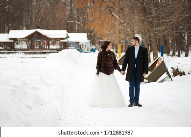 The Bride And Groom Fight Hands And Stroll Through The Winter Park. Winter Wedding.