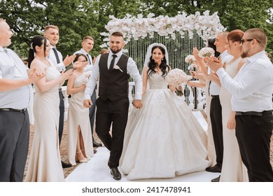 Bride and groom with friends near the ceremonial arch. Friends support the bride and groom. Lush and elegant bride's dress. Stylish wedding. Summer wedding in nature. - Powered by Shutterstock