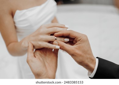 A bride and groom are getting married and exchanging rings. The bride is wearing a white dress and the groom is wearing a suit. Scene is happy and celebratory - Powered by Shutterstock