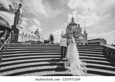 Bride And Groom Go To Church On Wedding Day. Wedding Couple Holding Hands And Going Up The Stairs Of The Castle. Back View. Black And White Photo.