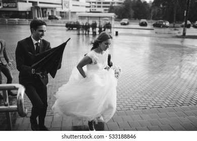 The Bride And Groom Go Under Rain. Rainy Wedding Day.