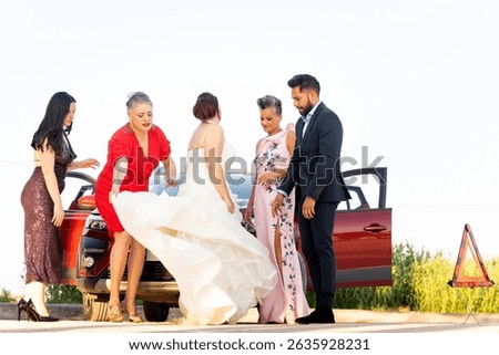 Bride, groom, and guests are fixing a problem with their car on the side of the road during a wedding