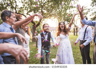Bride, groom and guests throwing confetti at wedding reception outside.