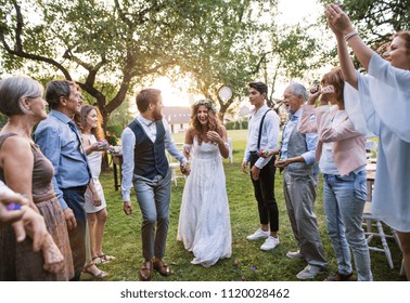 Bride, Groom And Guests At Wedding Reception Outside In The Backyard.