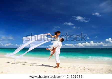 Bride and groom having fun on white sandy tropical beach. Beach wedding concept