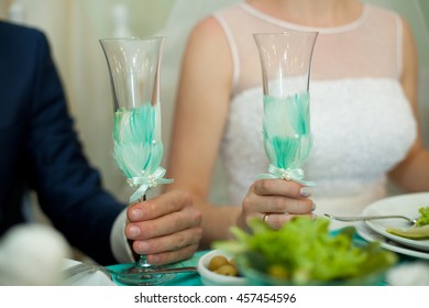 Bride And Groom Hold Champagne Flutes Decorated With Mint Feathers
