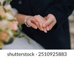 A bride and groom are holding hands in front of a bouquet of flowers. The bride is wearing a white dress and the groom is wearing a black suit. Scene is romantic and happy