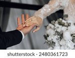 A bride and groom are holding hands, with the bride wearing a white dress and the groom wearing a wedding ring