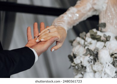 A bride and groom are holding hands, with the bride wearing a white dress and the groom wearing a wedding ring - Powered by Shutterstock