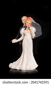 Bride And Groom Holding An Old Cake Topper On A Black Background. Figurines For A Wedding Cake. Figures Of Newlyweds In Festive Costumes.