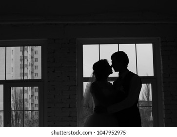 bride and groom kiss in the dark room near the window, silhouetted