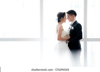 A bride and groom kissing over large bright window.