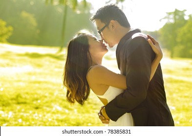 Bride and groom kissing in the park, back-lit in the morning.