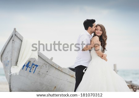 Bride and groom kissing at a photo session, near a boat close to the sea