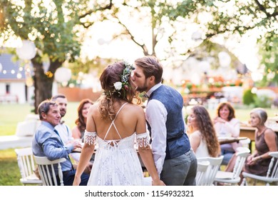 Bride And Groom Kissing At Wedding Reception Outside In The Backyard.