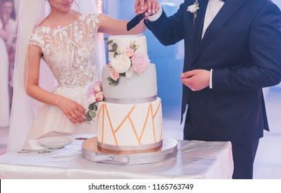 Bride And Groom In Love Cutting Beautiful Three Tiered Modern Tasty Wedding Cake With A Big Knife At Their Wedding Reception Party