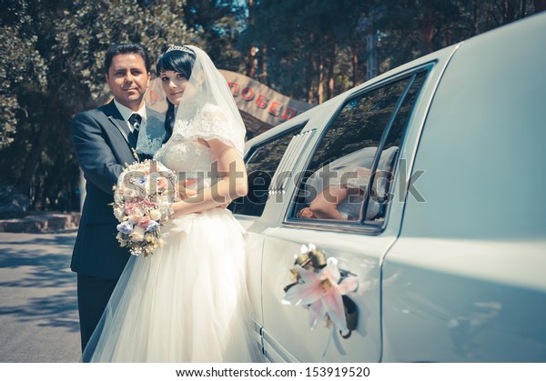 bride\
and groom near the limousine with wedding\
bouquet