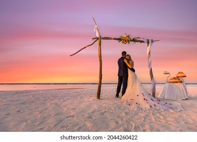Bride and groom, newlyweds, honeymoon on the beach sunset sun under wedding arch with cake. Lovers or newlywed married young couple by the sea, wedding ceremony on a tropical beach, ocean background - Powered by Shutterstock