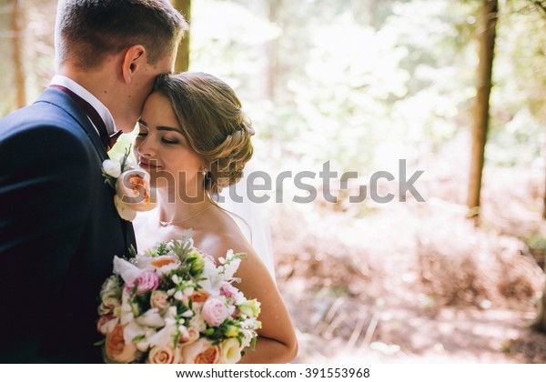 自然の緑の森の結婚式で 新郎新婦の新郎新婦が 写真のポートレートにキスをしています 結婚式 の写真素材 今すぐ編集