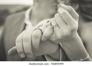 Bride and groom pinky swear closeup of hands and fingers crossed kissing in background black and white
