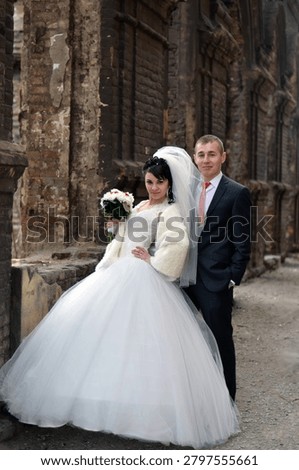 A bride and groom posing in front of old architectural ruins, creating a dramatic and cinematic wedding editorial scene. The contrast between elegant wedding attire and historic decay emphasizes timeless love, heritage, and emotional storytelling.