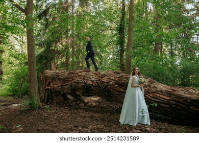 A bride and groom are posing for a picture on a log in the woods. Scene is romantic and intimate, as the couple is surrounded by nature and the log serves as a unique - Powered by Shutterstock