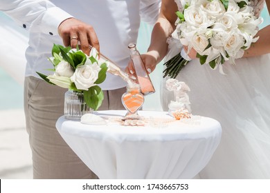 Bride And Groom Pouring Colorful Different Colored Sands Into The Crystal Vase Close Up During Symbolic Nautical Decor Destination Wedding Marriage Unity Ceremony On Sandy Beach In Front Of The Ocean 