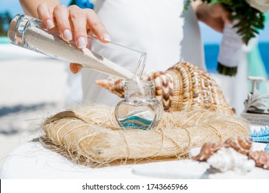 Bride And Groom Pouring Colorful Different Colored Sands Into The Crystal Vase Close Up During Symbolic Nautical Decor Destination Wedding Marriage Unity Ceremony On Sandy Beach In Front Of The Ocean 