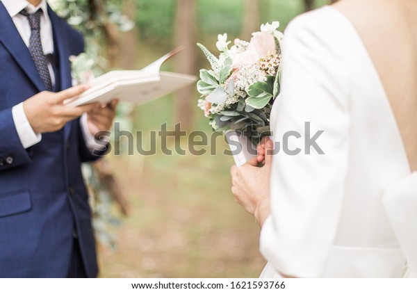 Bride and groom reading wedding vows from paper\
at wedding ceremony in\
nature.
